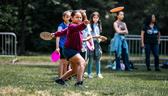 Children lined up, taking turns throwing discs