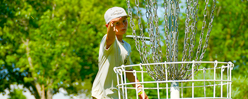 A child throwing his disc into the basket from within arms reach