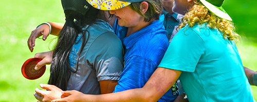 A group of children hugging as they play disc golf