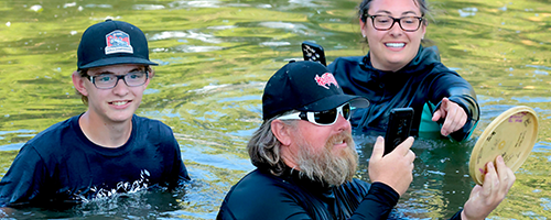 A group of people in a lake, smiling after finding a disc in the water